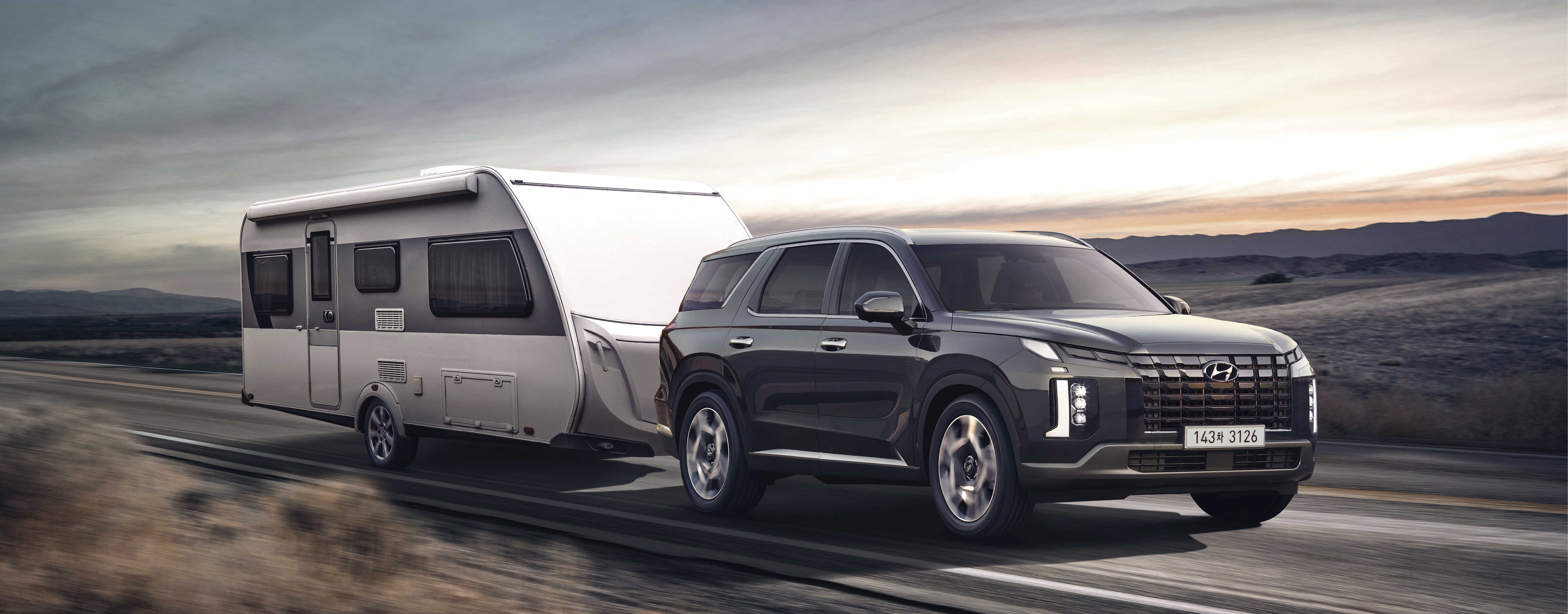 A black palisade driving a caravan on a one-way asphalt road