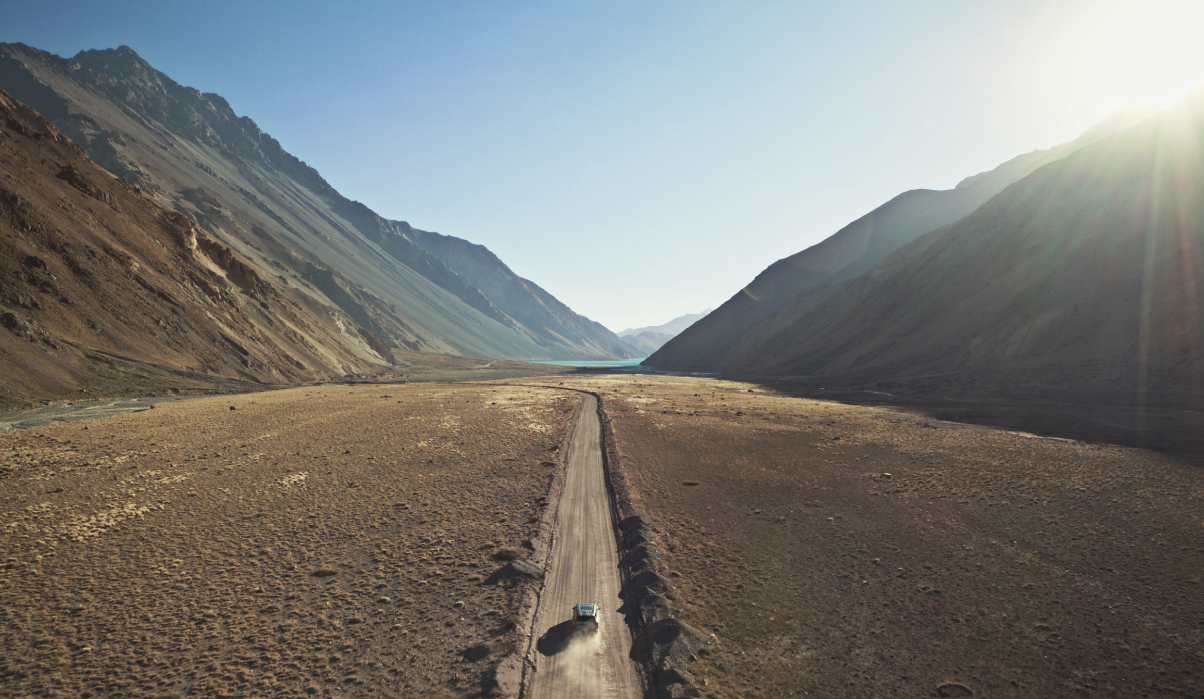 A car is driving on a road in the middle of a wide open natural landscape