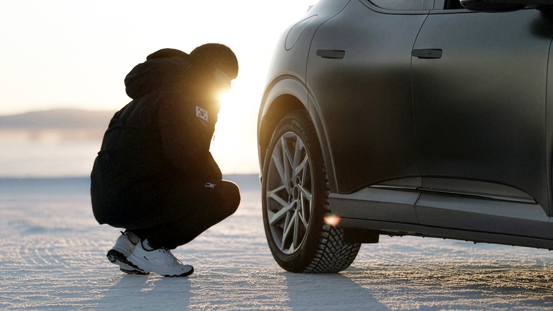 A staff member inspecting tires beside a snow-covered vehicle