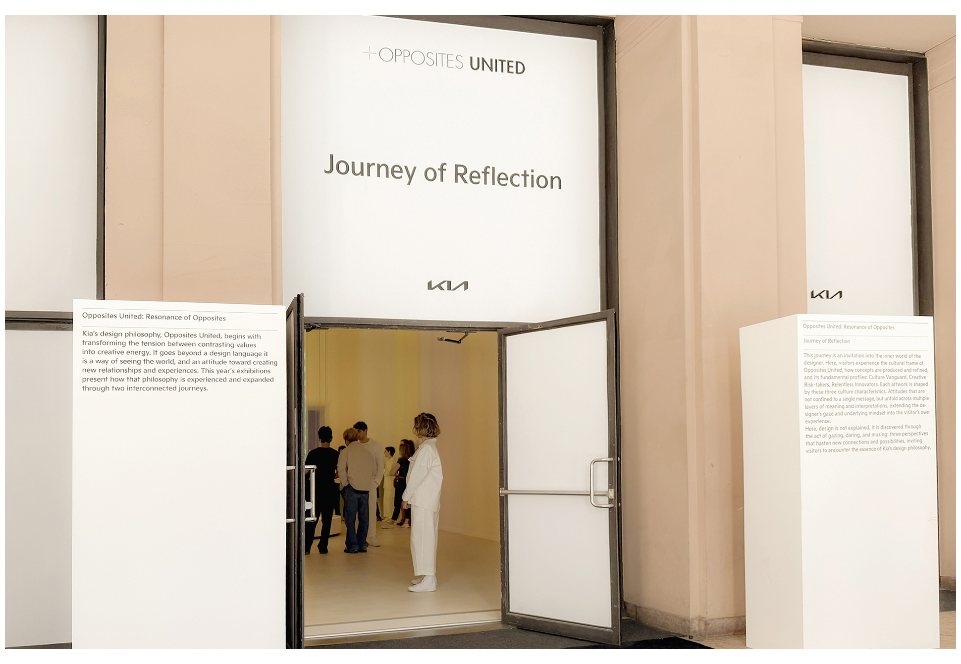 A large frame structure installed at the center of a beige-toned exhibition space with visitors