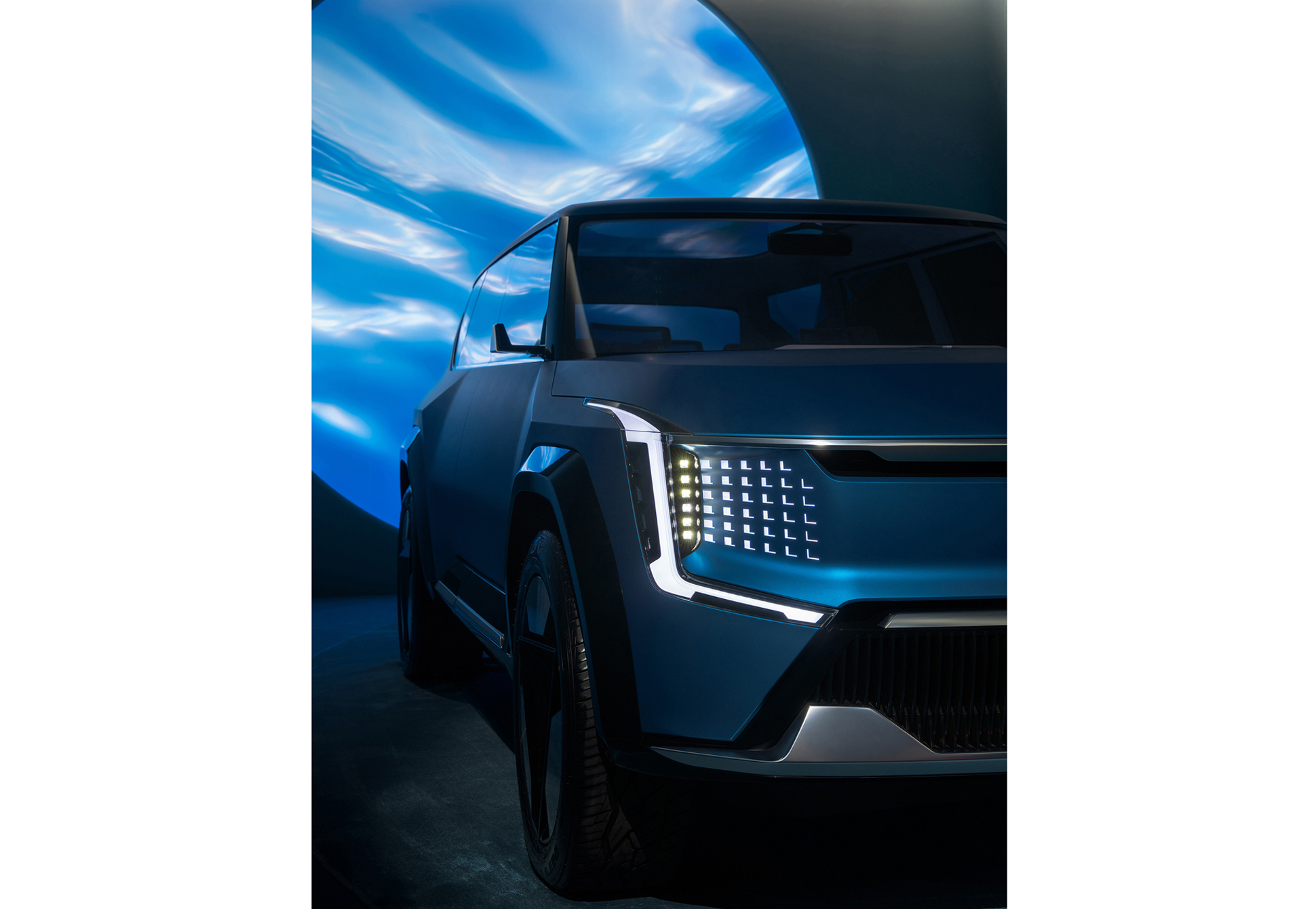An SUV on display inside an exhibition hall with a circular graphic projected on the wall behind it (EV9)