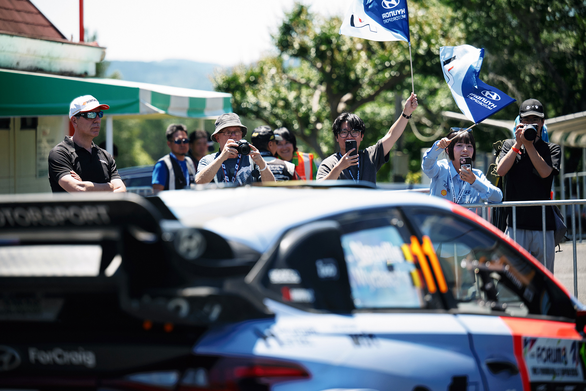 Hyundai N race cars lined up in the pit lane with cheering fans nearby