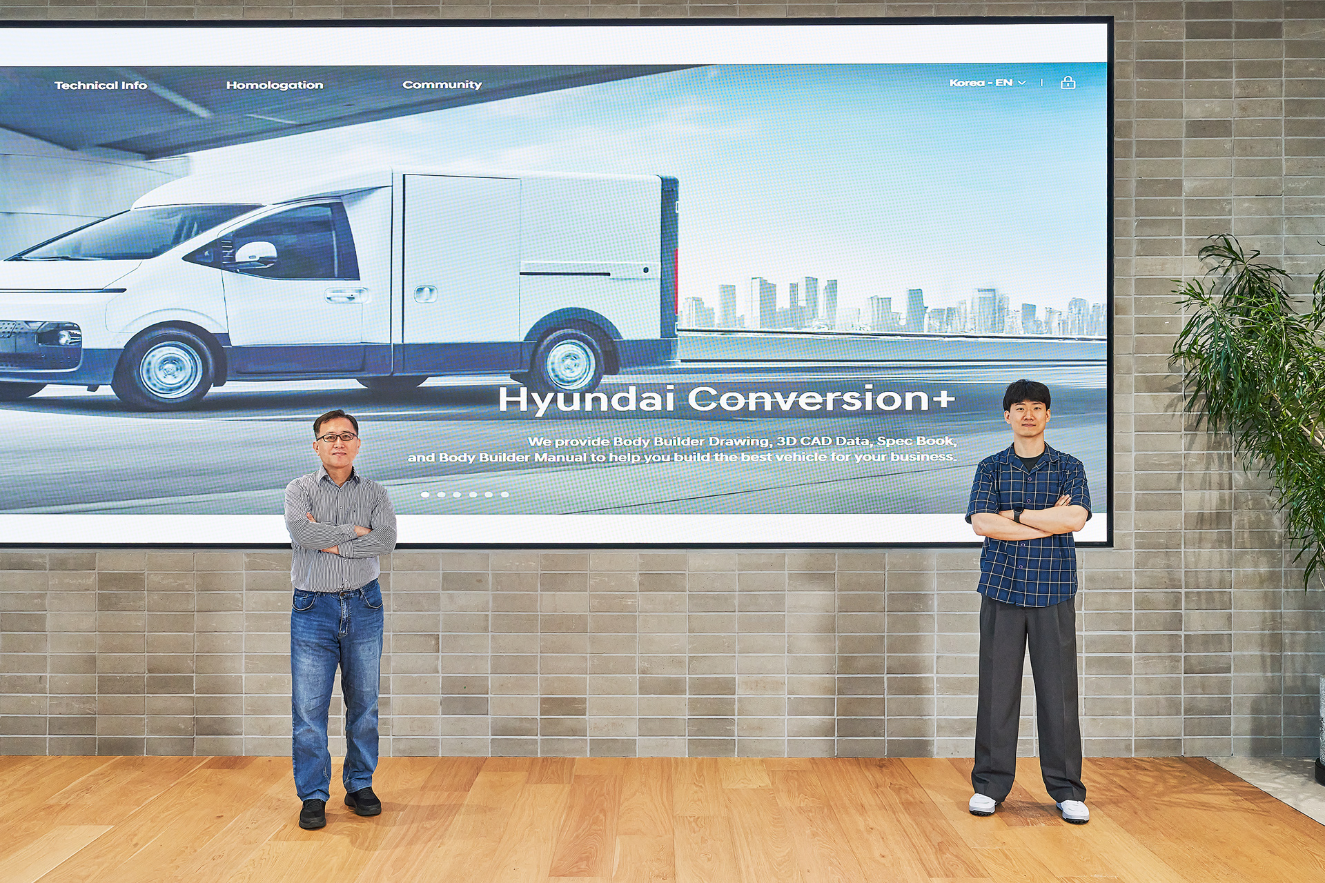 Minseop Jung and Seungjin Jeong posing in front of a large digital screen displaying a special-purpose vehicle