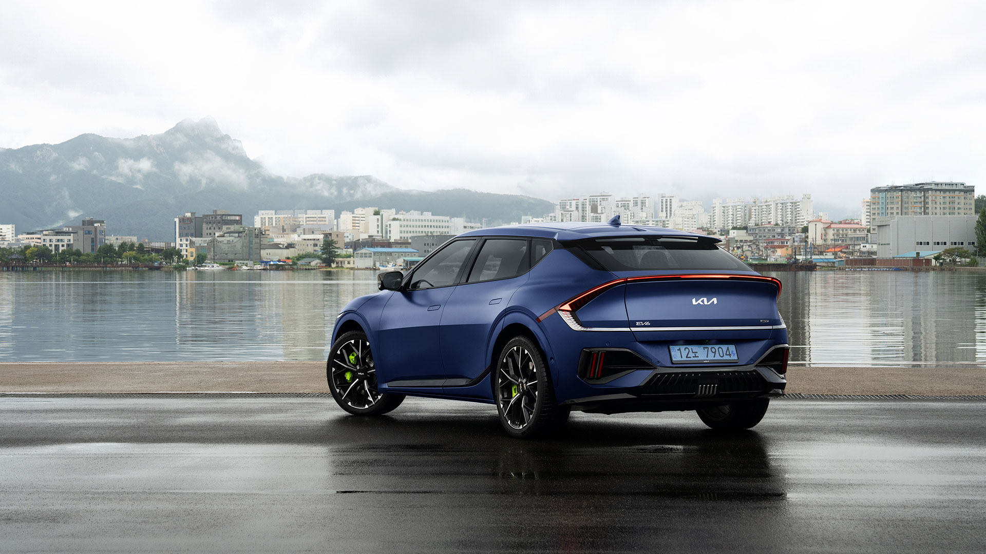 Rear view and rear light bar of a matte blue EV6 GT parked on the wet pavement of a harbor pier