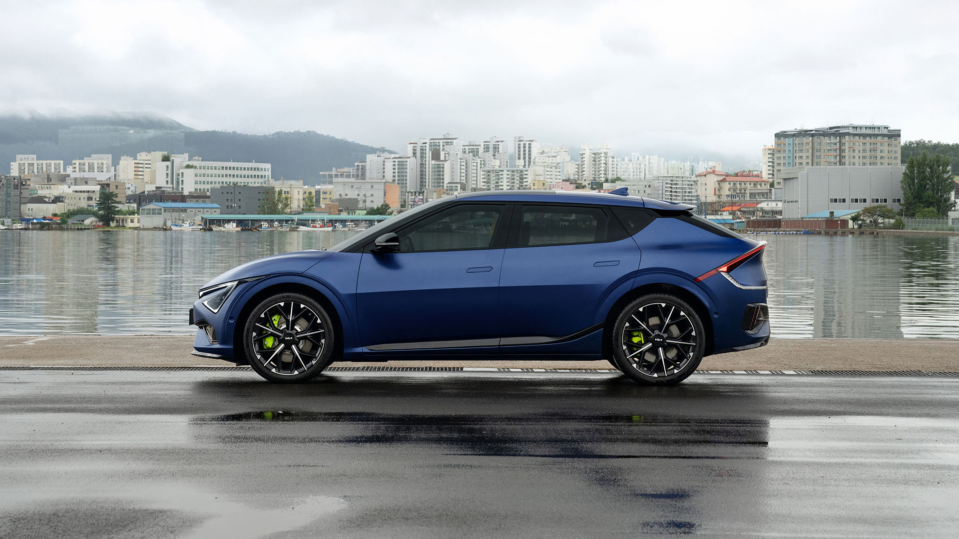 Side view of a matte blue EV6 GT parked on a rain-soaked pier, with neon-colored brake calipers